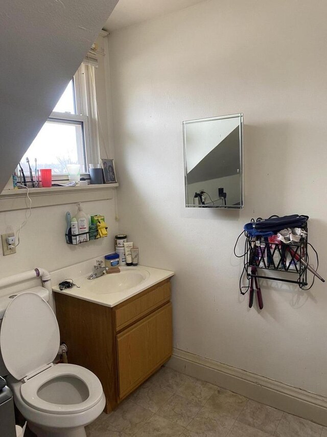 half bathroom with baseboards, toilet, and vanity