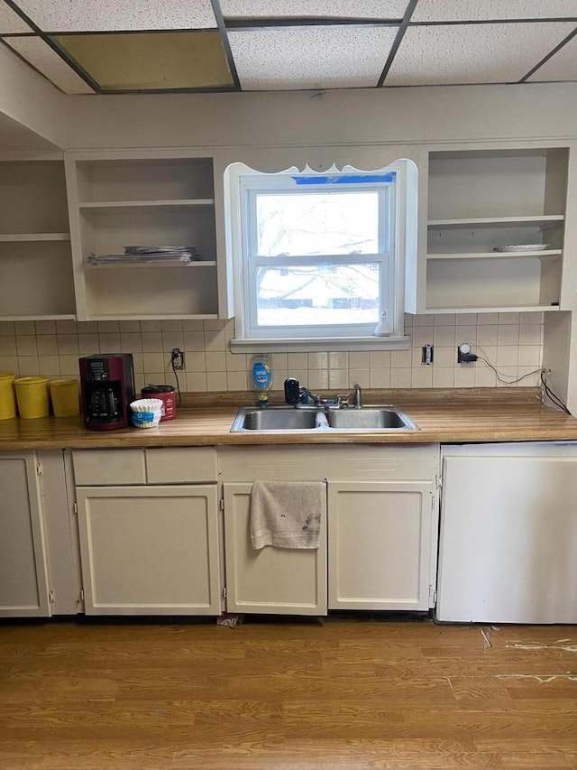 kitchen with open shelves, wood finished floors, a sink, and backsplash