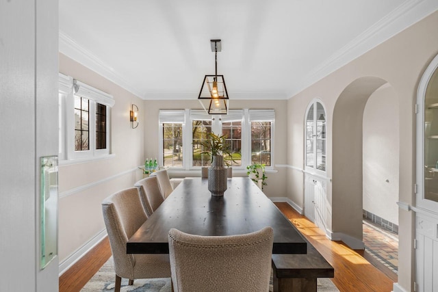 dining space featuring crown molding, arched walkways, a healthy amount of sunlight, and wood finished floors
