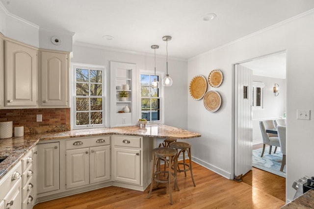 kitchen with crown molding, light stone counters, light wood finished floors, decorative light fixtures, and decorative backsplash