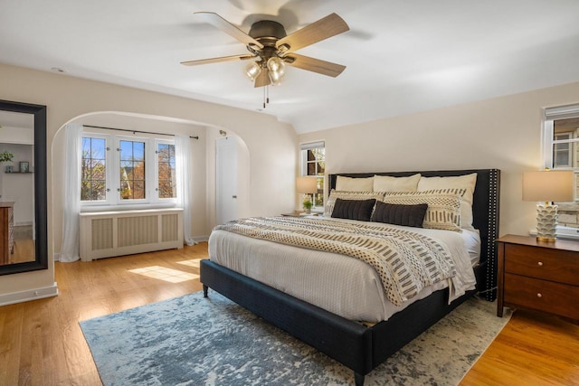 bedroom with arched walkways, a ceiling fan, wood finished floors, and radiator