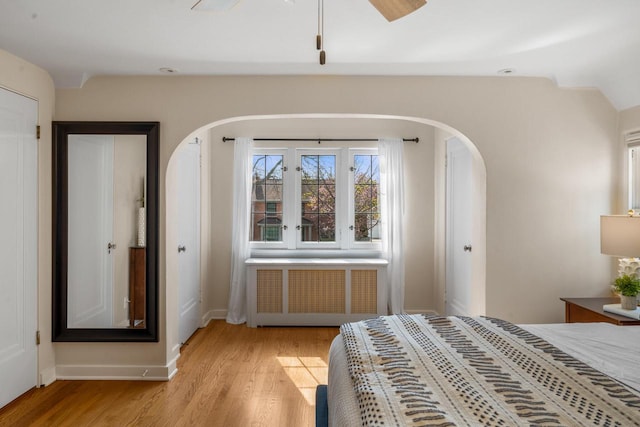 bedroom with arched walkways, baseboards, radiator, and light wood finished floors