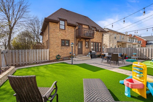 rear view of house featuring brick siding, a fenced backyard, a balcony, and a patio