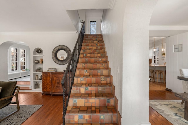 stairs featuring arched walkways, ornamental molding, and wood finished floors