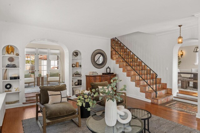 living room with arched walkways, built in shelves, wood finished floors, stairway, and ornamental molding