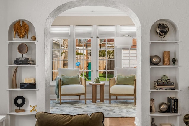 living area featuring built in features, arched walkways, crown molding, and wood finished floors