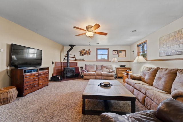 living room featuring a wood stove, ceiling fan, and carpet