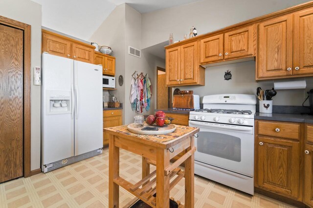 kitchen featuring visible vents, brown cabinetry, white appliances, and light floors