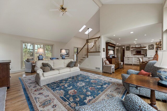 living room featuring a ceiling fan, visible vents, stairway, high vaulted ceiling, and light wood-style flooring