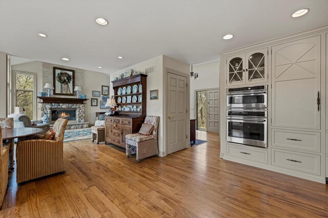 living room featuring recessed lighting, visible vents, a stone fireplace, and light wood-style flooring