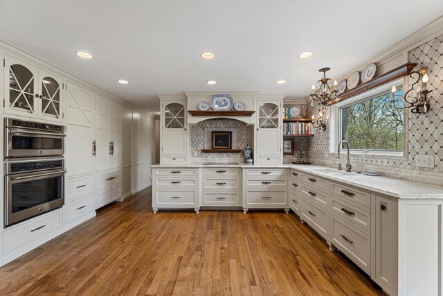 kitchen featuring an inviting chandelier, a sink, tasteful backsplash, and glass insert cabinets