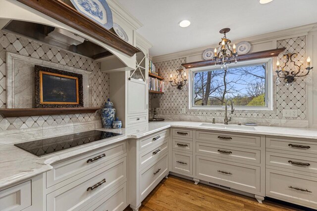 kitchen featuring decorative backsplash, black electric stovetop, custom range hood, a sink, and a notable chandelier