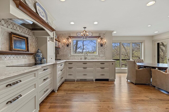 kitchen featuring decorative backsplash, an inviting chandelier, black electric stovetop, and a sink