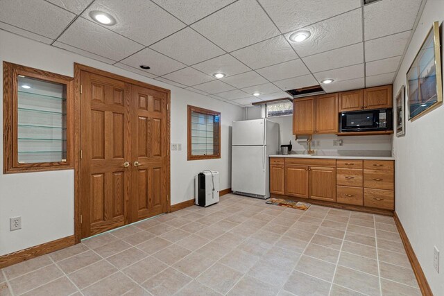 kitchen featuring black microwave, light countertops, brown cabinetry, freestanding refrigerator, and baseboards