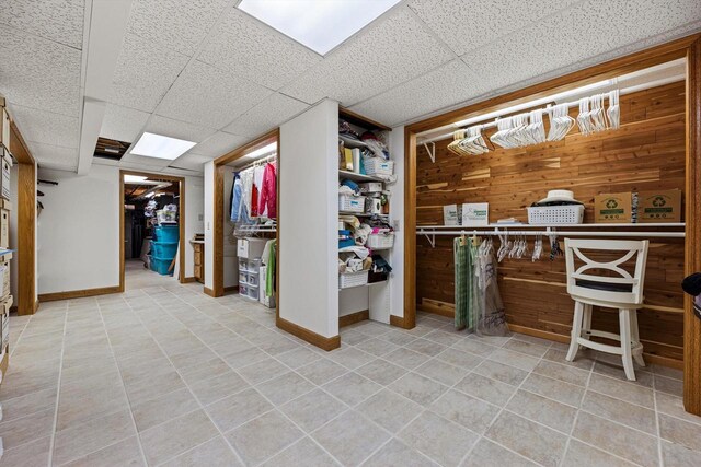 interior space with baseboards, light tile patterned floors, a drop ceiling, and wooden walls