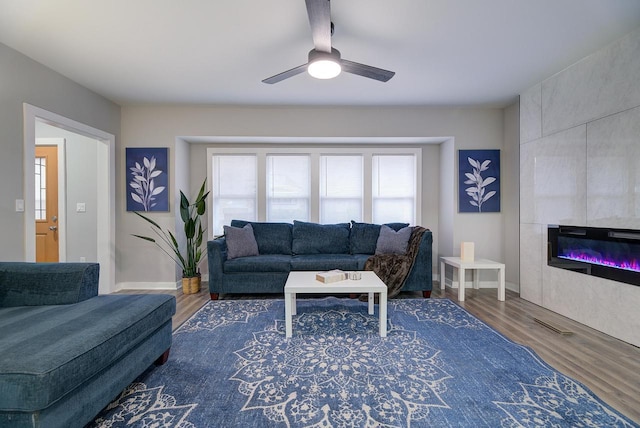 living area featuring a wealth of natural light, a tiled fireplace, wood finished floors, and ceiling fan