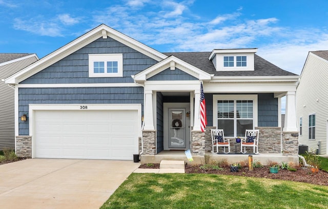 craftsman house featuring a shingled roof, stone siding, covered porch, and driveway
