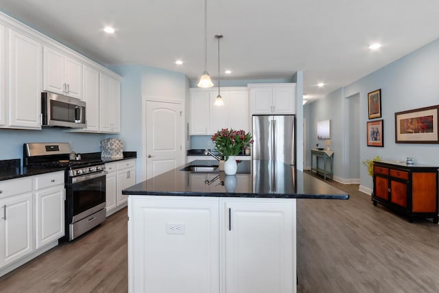 kitchen with white cabinetry, a center island with sink, wood finished floors, and stainless steel appliances