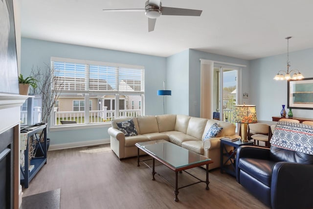 living area featuring visible vents, ceiling fan with notable chandelier, baseboards, and wood finished floors