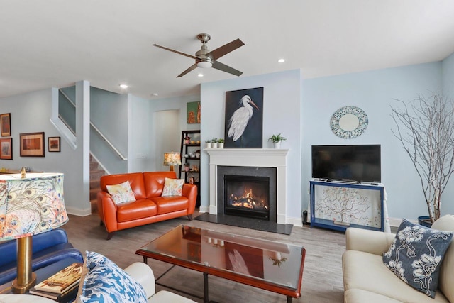 living area with a ceiling fan, a warm lit fireplace, recessed lighting, stairway, and baseboards