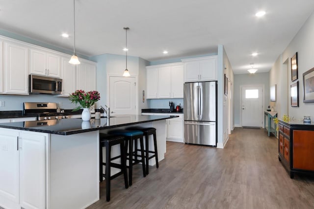 kitchen with dark countertops, a center island with sink, white cabinetry, and appliances with stainless steel finishes
