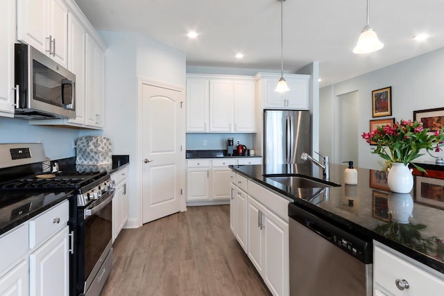 kitchen with white cabinets, light wood-style floors, stainless steel appliances, pendant lighting, and a sink