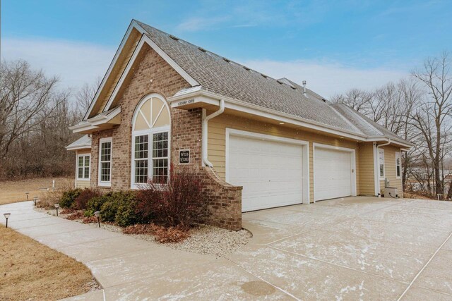 W209N11385 Reger Ct, Germantown, WI 53022 - view of side of property with brick siding, an attached garage, driveway, and roof with shingles