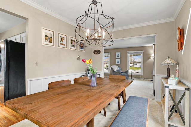 dining room featuring crown molding, light carpet, wainscoting, and a notable chandelier