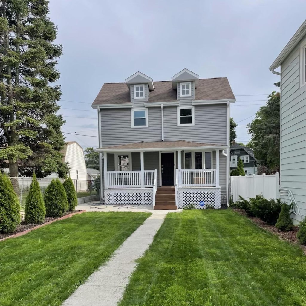 view of front facade with a shingled roof, a porch, fence, and a front lawn