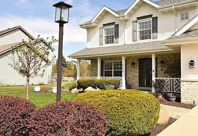 view of front of house featuring roof with shingles, a porch, and brick siding