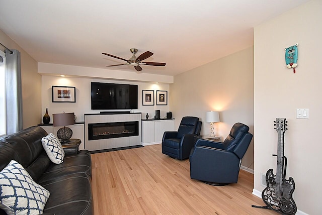 living room with ceiling fan, a glass covered fireplace, baseboards, and light wood-style floors