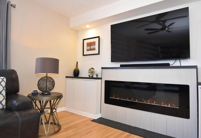 living area featuring baseboards, ceiling fan, a glass covered fireplace, and wood finished floors