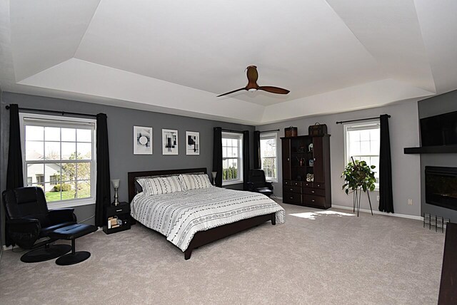 bedroom featuring a raised ceiling, baseboards, carpet, and ceiling fan