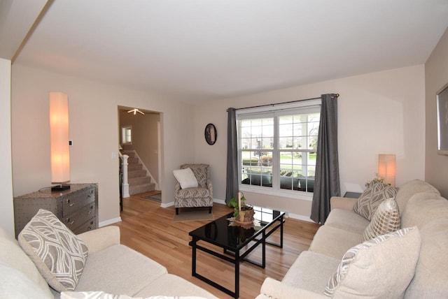 living room featuring baseboards, light wood-type flooring, and stairs
