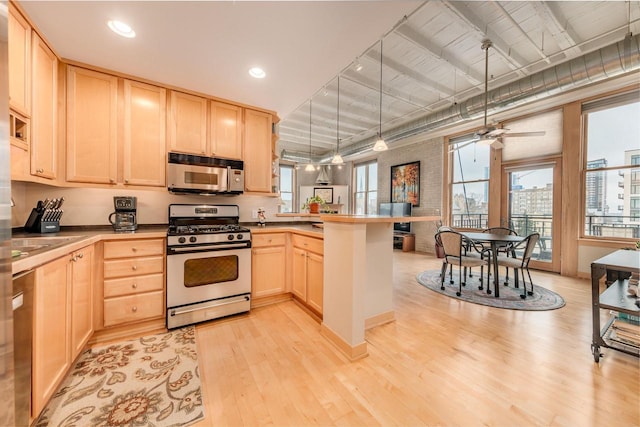 kitchen featuring a peninsula, light brown cabinetry, appliances with stainless steel finishes, hanging light fixtures, and light wood finished floors