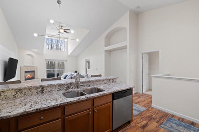 kitchen featuring high vaulted ceiling, stainless steel dishwasher, light stone countertops, a sink, and open floor plan