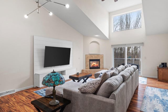 living area featuring visible vents, baseboards, a fireplace, wood finished floors, and high vaulted ceiling