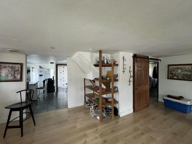hallway featuring a barn door, visible vents, baseboards, and wood finished floors