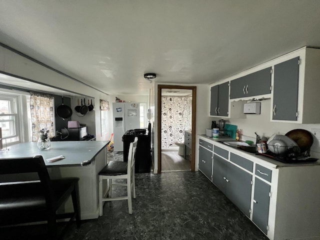kitchen with white fridge with ice dispenser, dark floors, a breakfast bar, light countertops, and a sink