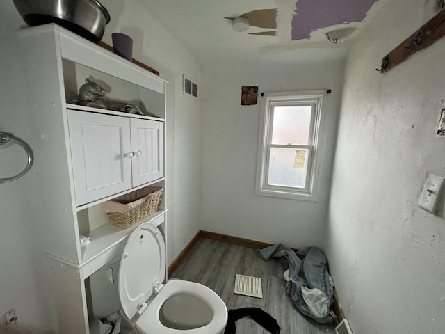 bathroom with toilet, wood finished floors, baseboards, and visible vents
