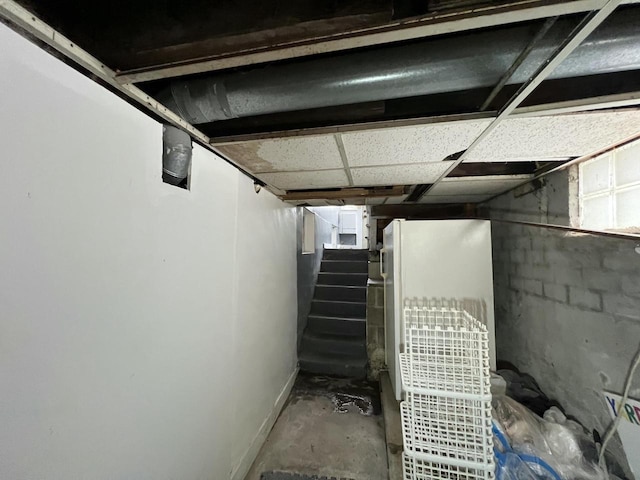 unfinished basement featuring stairway and freestanding refrigerator