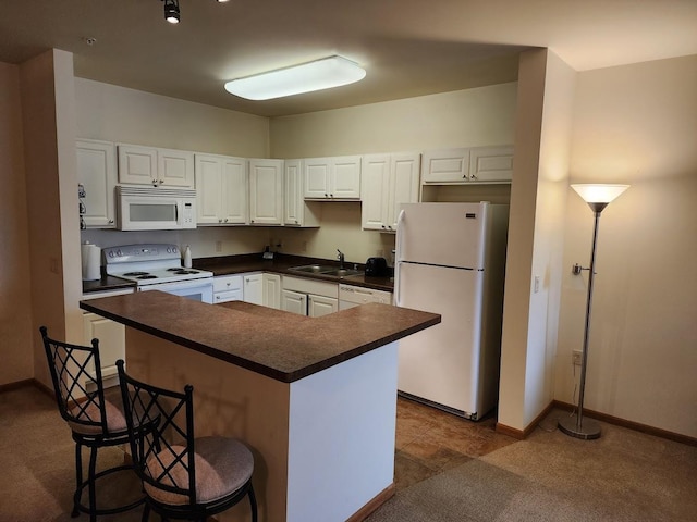 kitchen with white appliances, dark countertops, white cabinets, a breakfast bar area, and a sink