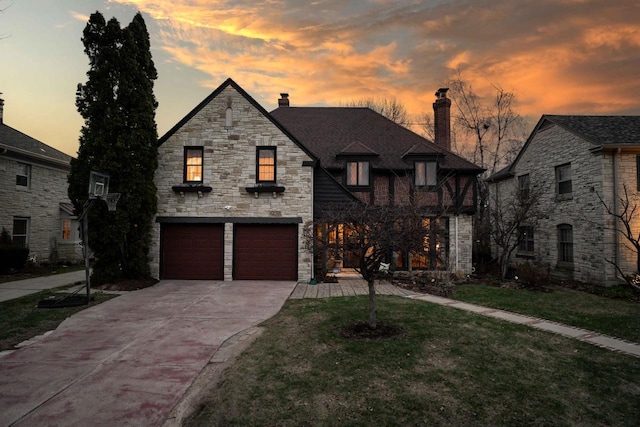 french provincial home featuring a garage, stone siding, a yard, a chimney, and driveway