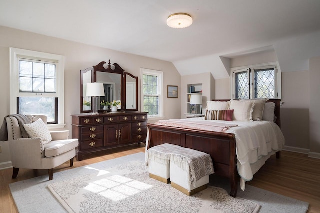 bedroom with baseboards, light wood-type flooring, and lofted ceiling