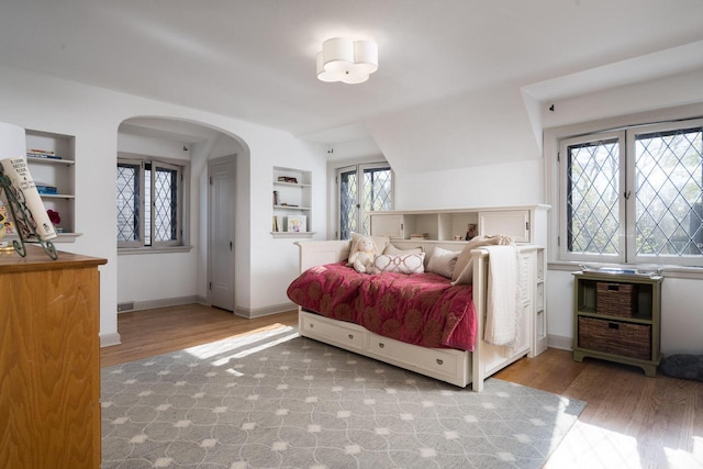 bedroom featuring arched walkways, baseboards, and wood finished floors