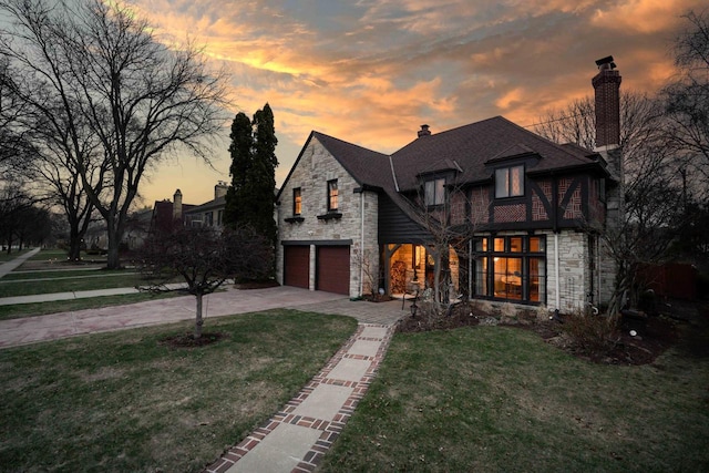 french country inspired facade featuring driveway, a chimney, stone siding, and a garage