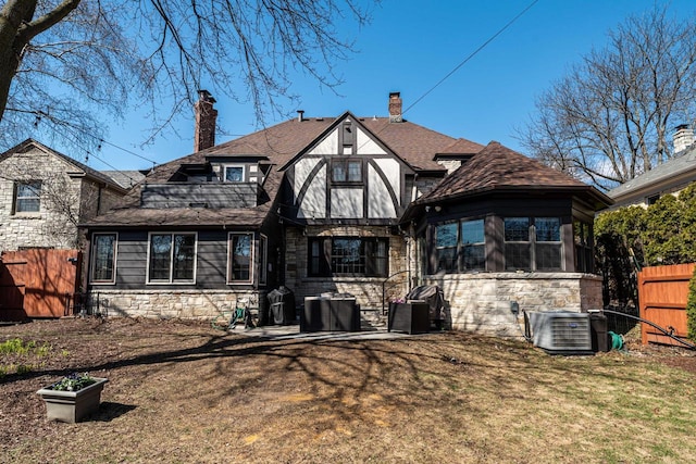 rear view of house with a lawn, fence, cooling unit, and stone siding