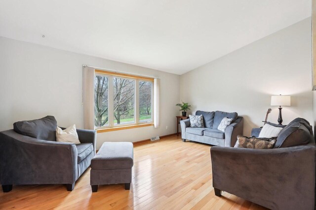 living area with baseboards, light wood finished floors, lofted ceiling, and visible vents