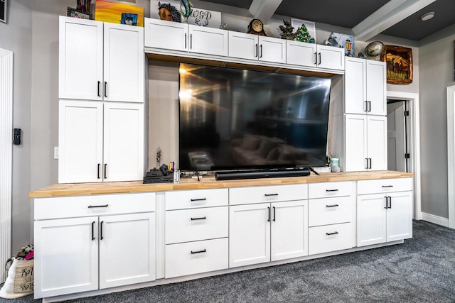 interior space featuring wooden counters, dark colored carpet, and white cabinets
