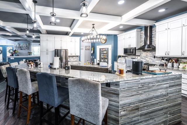kitchen featuring tasteful backsplash, a large island, wall chimney exhaust hood, coffered ceiling, and appliances with stainless steel finishes